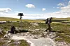 To vandrere i et steinete fjellandskap med skiltstolpe og blå himmel.