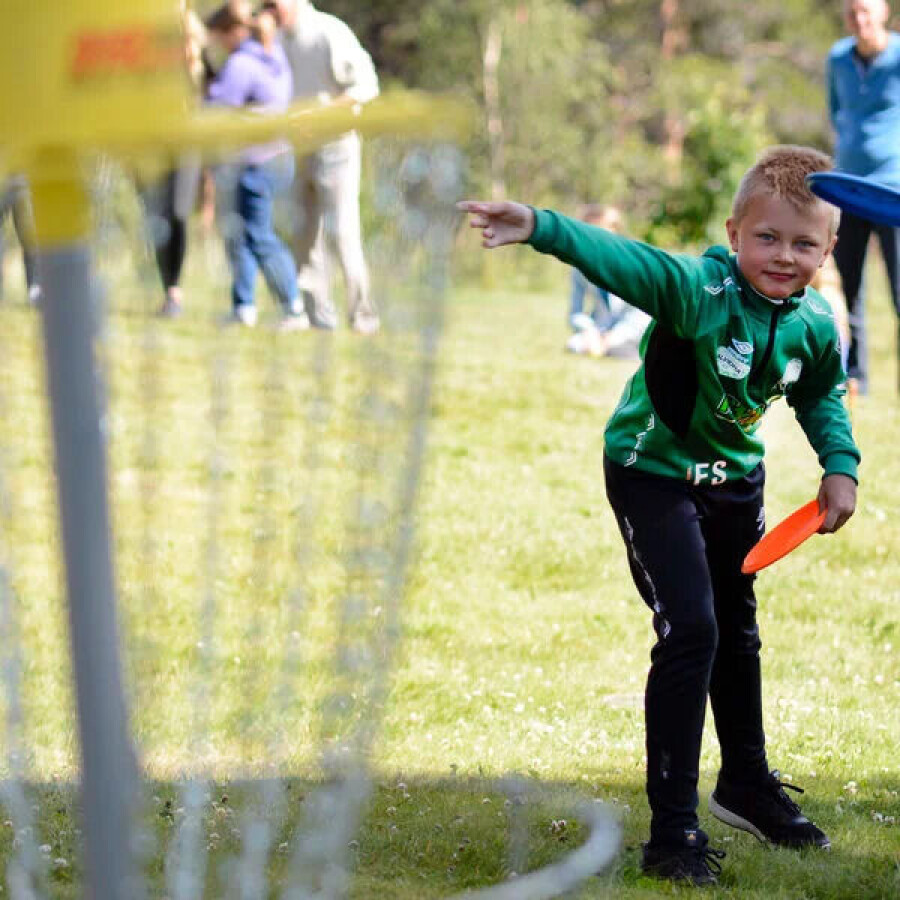 Ung gutt i grønn trøye kaster frisbee på en gressplen