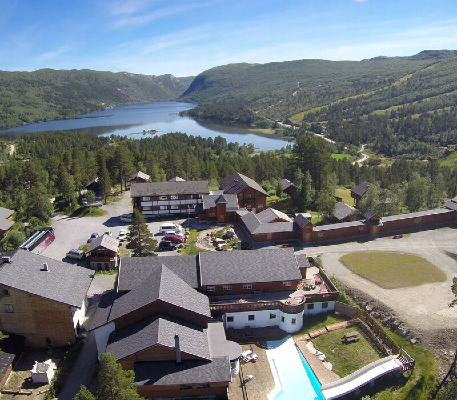 Hotellbygninger med basseng, omgitt av skog og fjell ved en innsjø